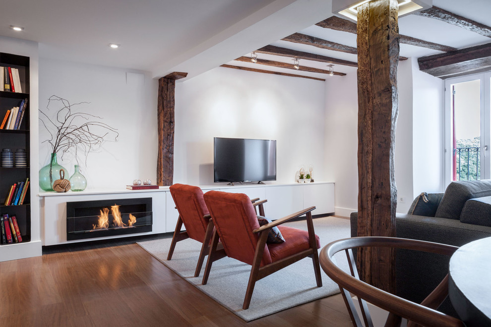 Photo of a mid-sized mediterranean open concept family room in Bilbao with white walls, medium hardwood floors, a ribbon fireplace, a metal fireplace surround, a freestanding tv and brown floor.
