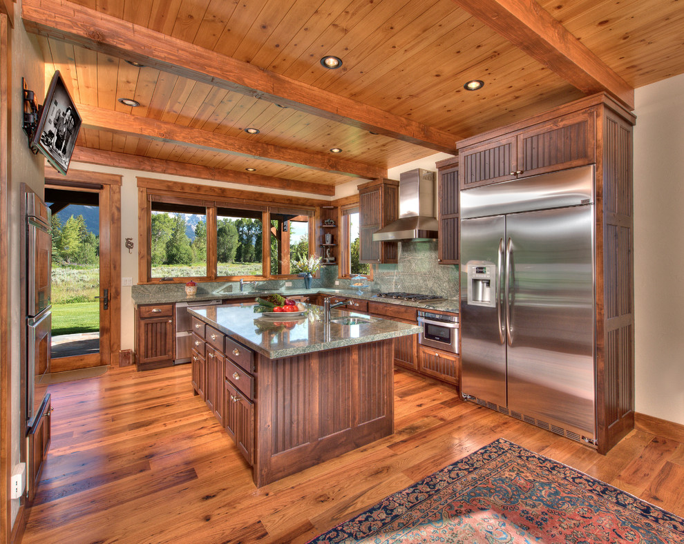 Mountain style u-shaped medium tone wood floor enclosed kitchen photo with an island, an undermount sink, recessed-panel cabinets, dark wood cabinets, stainless steel appliances and gray countertops