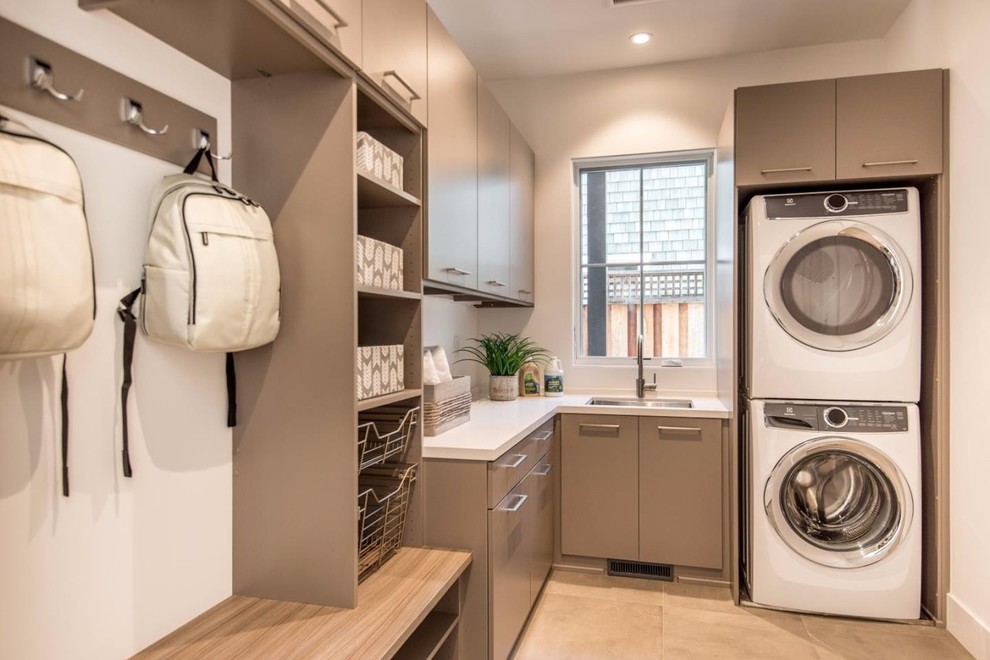 Inspiration for a mid-sized modern l-shaped dedicated laundry room in San Francisco with an undermount sink, flat-panel cabinets, brown cabinets, quartz benchtops, white walls, porcelain floors, a stacked washer and dryer, beige floor and white benchtop.