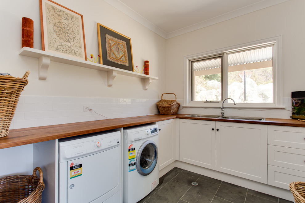 Inspiration for a mid-sized traditional l-shaped utility room in Adelaide with a double-bowl sink, shaker cabinets, wood benchtops, white walls, slate floors and a side-by-side washer and dryer.