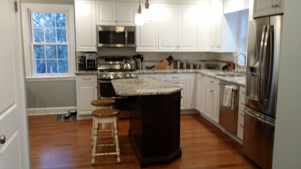 Example of a mid-sized transitional l-shaped light wood floor eat-in kitchen design in Baltimore with an undermount sink, raised-panel cabinets, white cabinets, granite countertops, white backsplash, stone tile backsplash, stainless steel appliances and an island