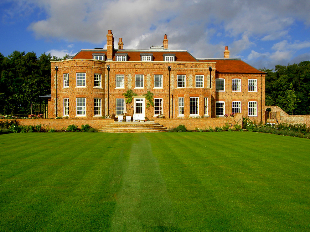This is an example of an expansive traditional three-storey brick red exterior in Hampshire with a hip roof.