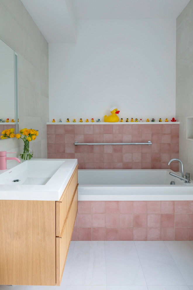 Modern inredning av ett mellanstort badrum för barn, med släta luckor, skåp i ljust trä, ett badkar i en alkov, rosa kakel, keramikplattor, ett integrerad handfat och bänkskiva i kvarts