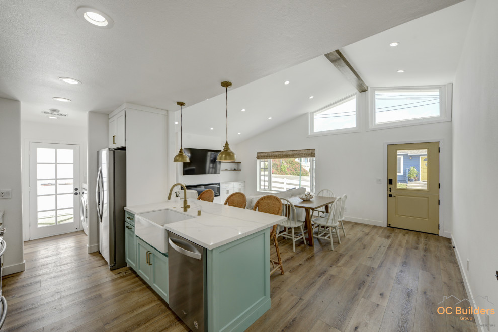 Photo of a medium sized coastal single-wall enclosed kitchen in Orange County with a belfast sink, shaker cabinets, turquoise cabinets, quartz worktops, white splashback, ceramic splashback, stainless steel appliances, medium hardwood flooring, an island, brown floors, white worktops and a vaulted ceiling.