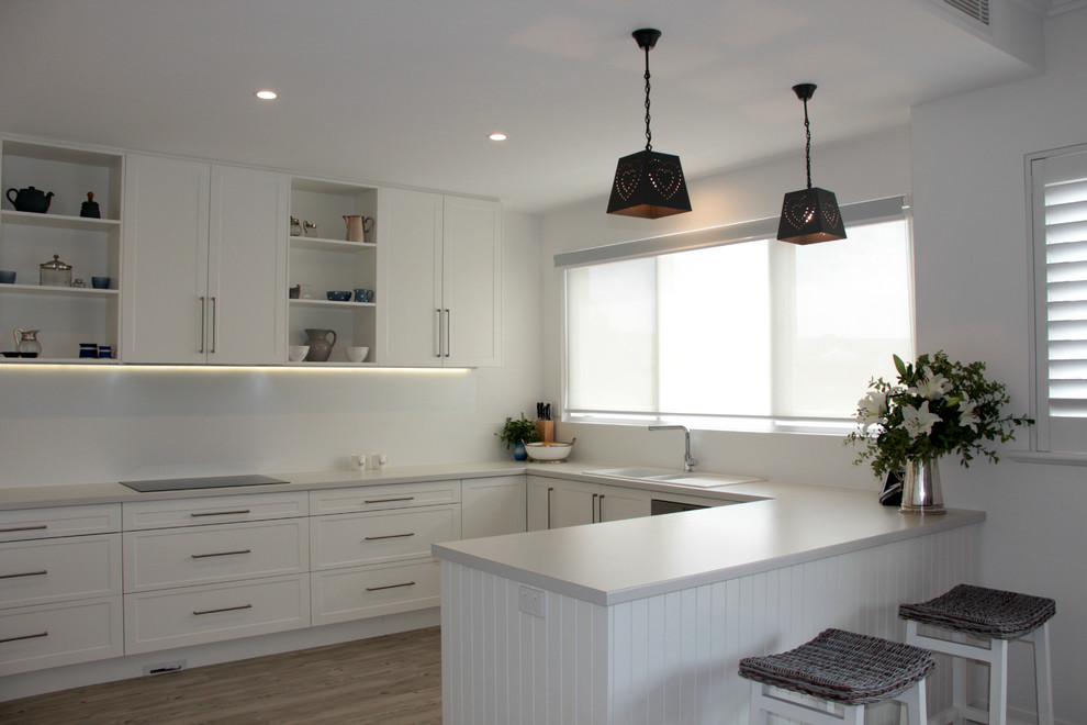 Design ideas for a mid-sized contemporary u-shaped open plan kitchen in Adelaide with shaker cabinets, white cabinets, solid surface benchtops, white splashback, stainless steel appliances, light hardwood floors and a peninsula.