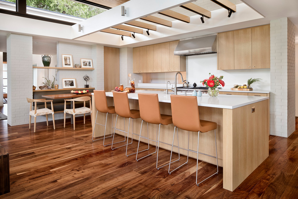 Large contemporary galley eat-in kitchen in Austin with an integrated sink, flat-panel cabinets, light wood cabinets, solid surface benchtops, white splashback, stainless steel appliances, medium hardwood floors and with island.