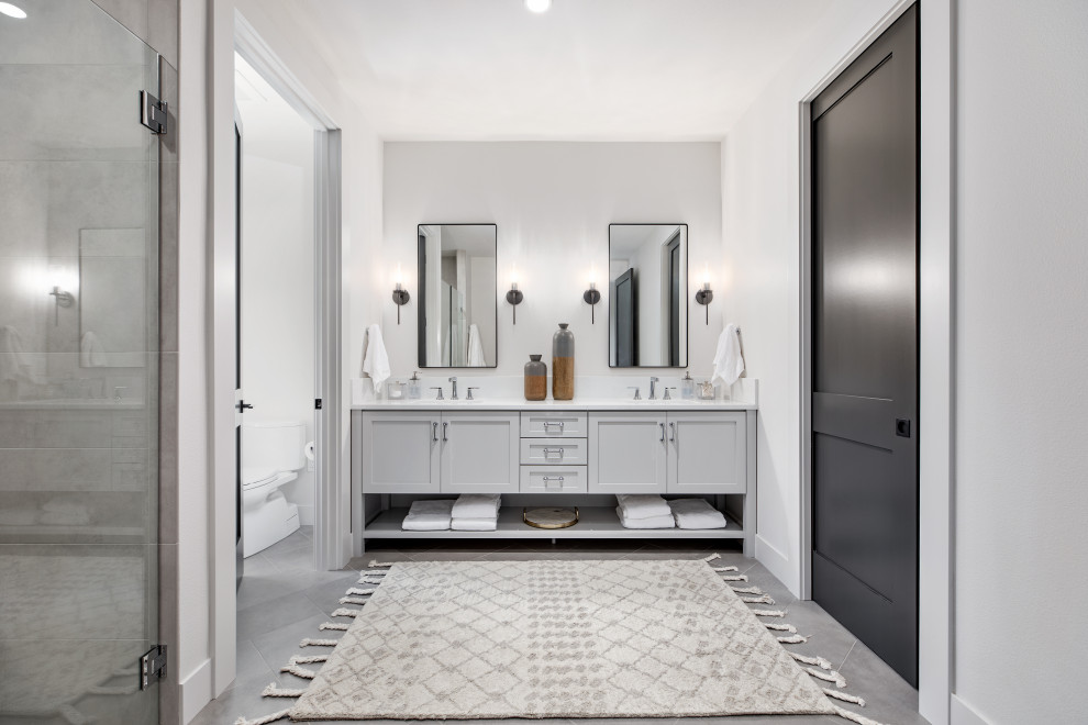 This is an example of a large country master wet room bathroom in Portland with shaker cabinets, grey cabinets, a one-piece toilet, white tile, ceramic tile, white walls, porcelain floors, a drop-in sink, engineered quartz benchtops, grey floor, a hinged shower door, white benchtops, an enclosed toilet, a double vanity, a built-in vanity and exposed beam.