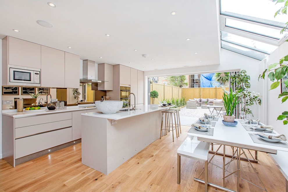 Photo of a large contemporary open plan kitchen in London with flat-panel cabinets, grey cabinets, quartzite benchtops, mirror splashback, stainless steel appliances, light hardwood floors, with island and an undermount sink.