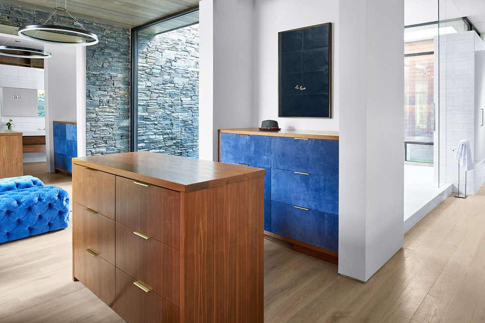 Photo of a large contemporary gender-neutral storage and wardrobe in Atlanta with flat-panel cabinets, light hardwood floors, blue cabinets and beige floor.