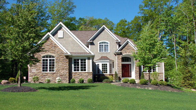 This is an example of a large traditional two-storey beige house exterior in Cleveland with stone veneer, a gable roof and a shingle roof.