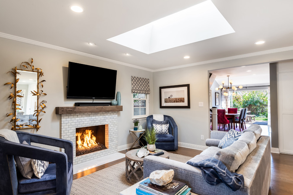 Photo of a transitional living room in Los Angeles with grey walls, medium hardwood floors, a standard fireplace, a tile fireplace surround, a wall-mounted tv and brown floor.