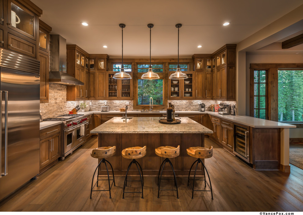 Inspiration for a large rustic u-shaped medium tone wood floor and brown floor open concept kitchen remodel with an undermount sink, raised-panel cabinets, brown cabinets, granite countertops, beige backsplash, travertine backsplash, stainless steel appliances and an island