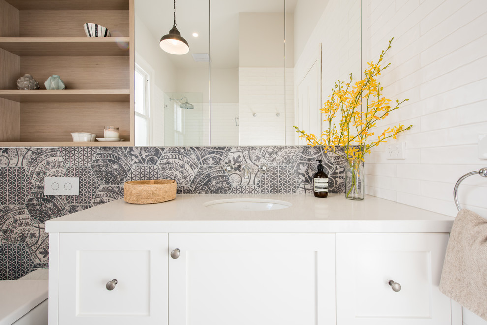 Inspiration for a mid-sized transitional bathroom in Melbourne with recessed-panel cabinets, white cabinets, engineered quartz benchtops, an undermount sink, a drop-in tub, a shower/bathtub combo, a wall-mount toilet, multi-coloured tile and porcelain floors.