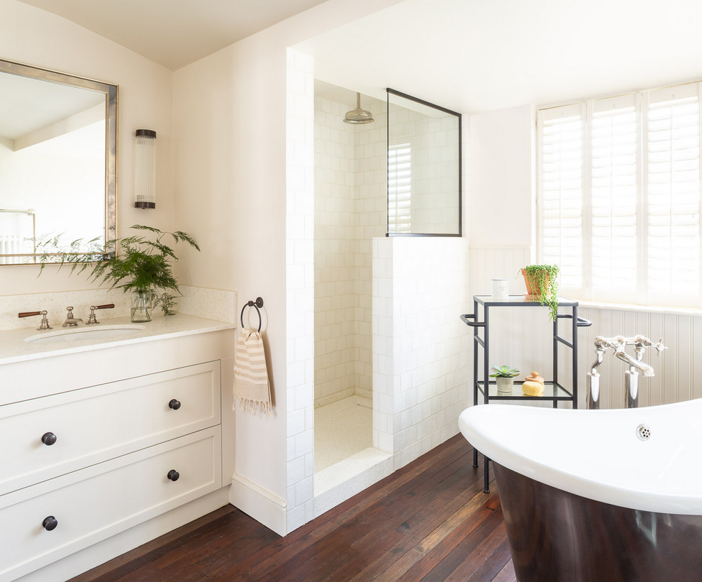 Photo of a transitional bathroom in London with shaker cabinets, white cabinets, a freestanding tub, an alcove shower, white walls, dark hardwood floors, an undermount sink, brown floor, an open shower and white benchtops.