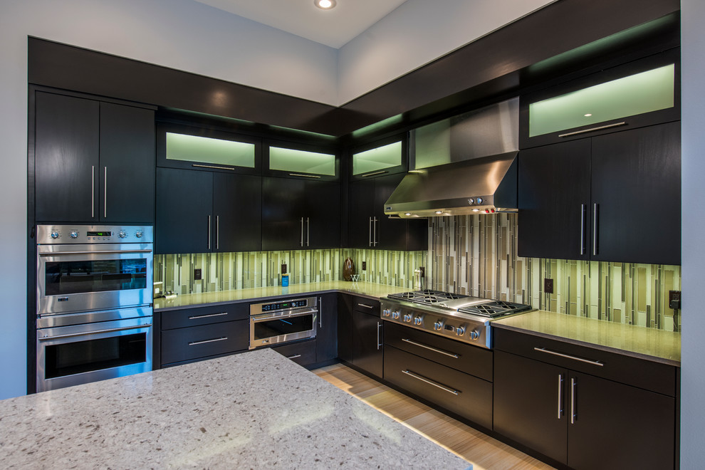 This is an example of a large modern l-shaped open plan kitchen in Other with flat-panel cabinets, dark wood cabinets, quartz benchtops, with island, an undermount sink, green splashback, glass tile splashback, panelled appliances and bamboo floors.