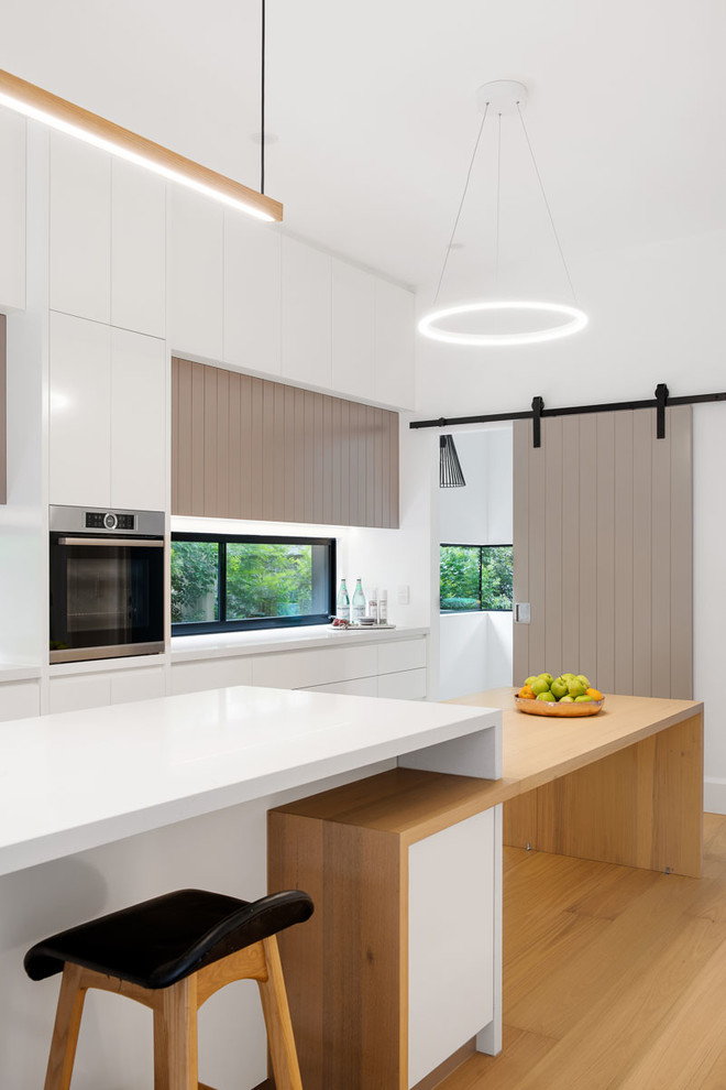 Kitchen in Melbourne with a double-bowl sink, grey cabinets, granite benchtops, glass sheet splashback, stainless steel appliances, light hardwood floors, multiple islands and white benchtop.