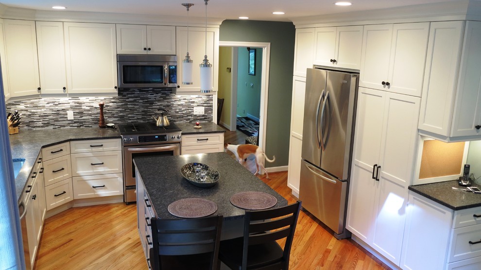 This is an example of a mid-sized transitional kitchen in Bridgeport with an undermount sink, white cabinets, glass tile splashback, stainless steel appliances, medium hardwood floors, with island, black benchtop, granite benchtops and grey splashback.