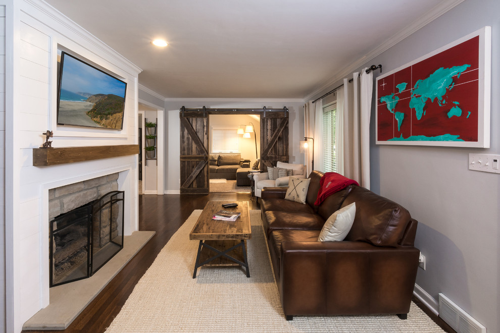 Photo of a mid-sized eclectic open concept living room in Columbus with grey walls, medium hardwood floors, a standard fireplace, a wood fireplace surround and a wall-mounted tv.