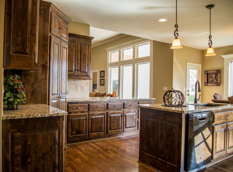 Design ideas for a mid-sized traditional l-shaped eat-in kitchen in Kansas City with an undermount sink, distressed cabinets, granite benchtops, beige splashback, stone tile splashback, black appliances, medium hardwood floors, with island and raised-panel cabinets.