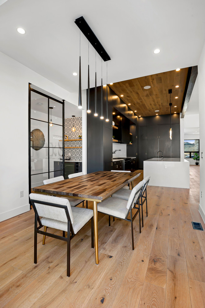 Cette image montre une grande salle à manger ouverte sur la cuisine minimaliste avec un mur blanc, parquet clair, un sol marron et poutres apparentes.