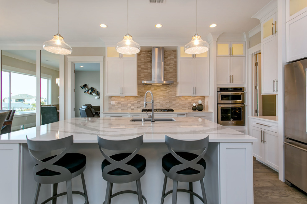 Photo of a large transitional l-shaped open plan kitchen in Seattle with an undermount sink, shaker cabinets, white cabinets, quartz benchtops, white splashback, marble splashback, stainless steel appliances, light hardwood floors, with island, grey floor and white benchtop.