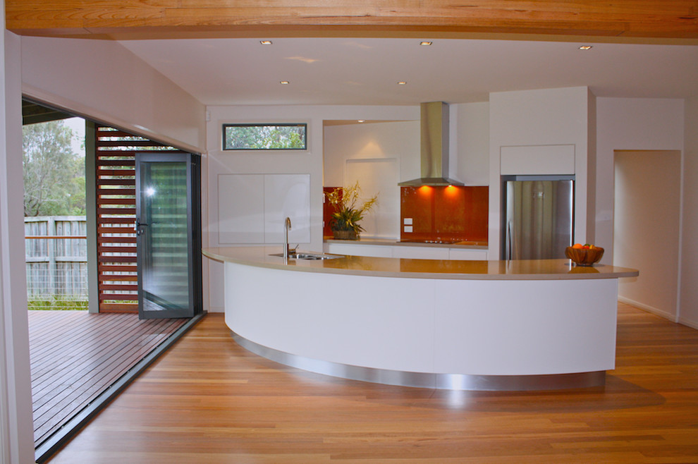 Design ideas for a small contemporary u-shaped kitchen pantry in Gold Coast - Tweed with a drop-in sink, flat-panel cabinets, white cabinets, quartz benchtops, red splashback, glass sheet splashback, stainless steel appliances, medium hardwood floors, with island and beige benchtop.