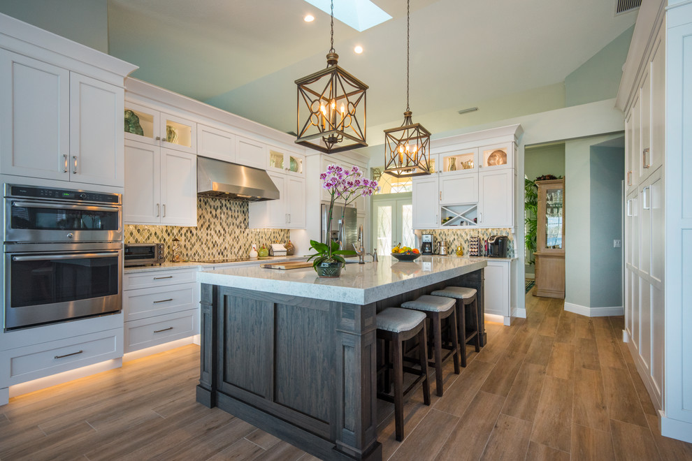 Design ideas for a large transitional l-shaped eat-in kitchen in Orlando with shaker cabinets, white cabinets, multi-coloured splashback, stainless steel appliances, medium hardwood floors, with island, brown floor, an undermount sink, quartzite benchtops and glass tile splashback.