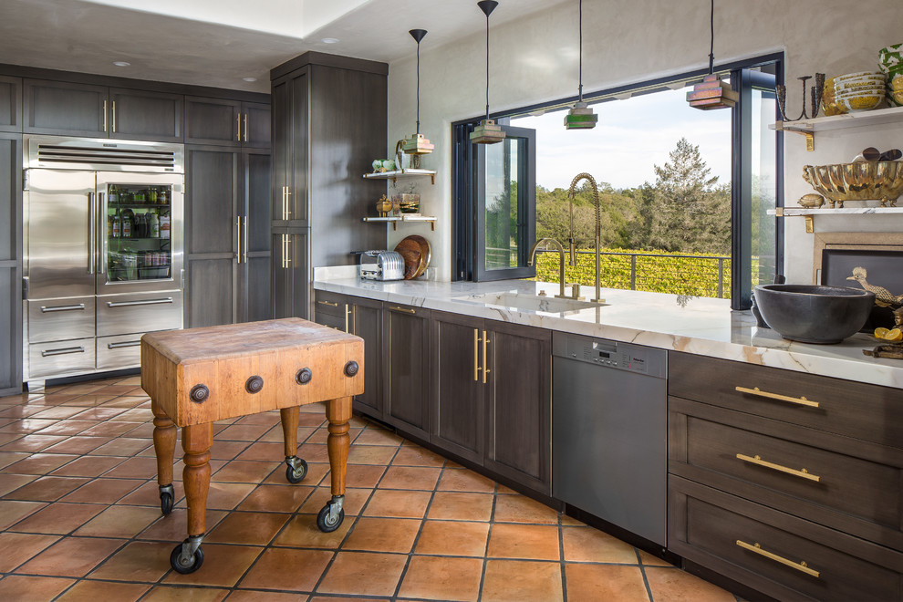 Photo of a large eclectic eat-in kitchen in San Francisco with an integrated sink, grey cabinets, marble benchtops, stainless steel appliances, terra-cotta floors, with island and shaker cabinets.