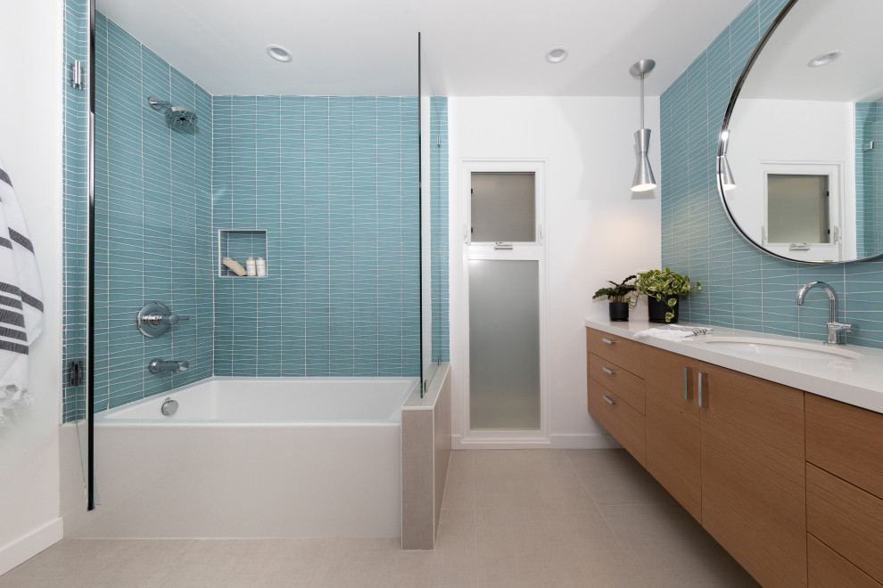 На фото: главная ванная комната среднего размера в стиле ретро с плоскими фасадами, коричневыми фасадами, накладной ванной, угловым душем, унитазом-моноблоком, синей плиткой, стеклянной плиткой, белыми стенами, полом из керамической плитки, врезной раковиной, столешницей из искусственного кварца, бежевым полом, душем с распашными дверями, белой столешницей, тумбой под одну раковину и подвесной тумбой
