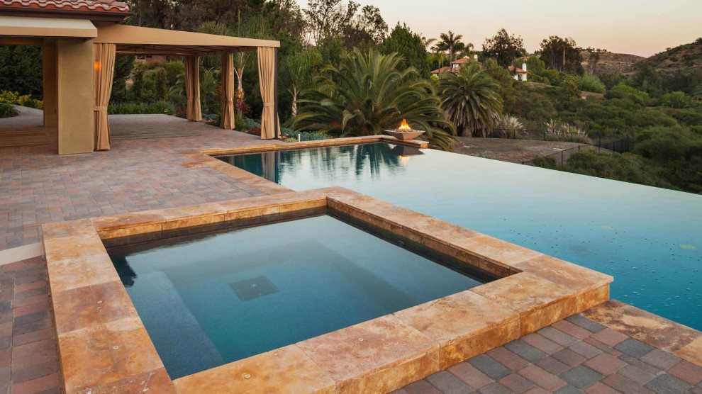 Inspiration for a mid-sized mediterranean backyard rectangular infinity pool in San Diego with a hot tub and brick pavers.