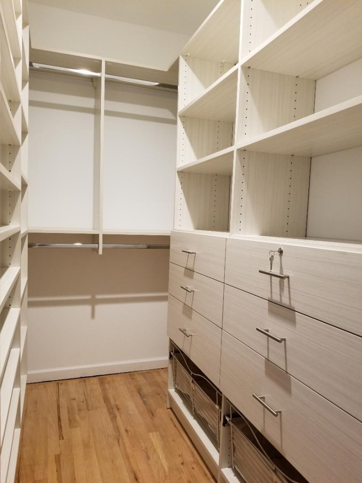 Large modern gender-neutral walk-in wardrobe in New York with flat-panel cabinets, light wood cabinets, light hardwood floors, beige floor and vaulted.
