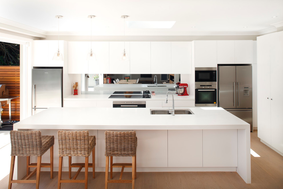 Contemporary kitchen in Sydney with flat-panel cabinets, white cabinets, mirror splashback, stainless steel appliances, light hardwood floors and with island.