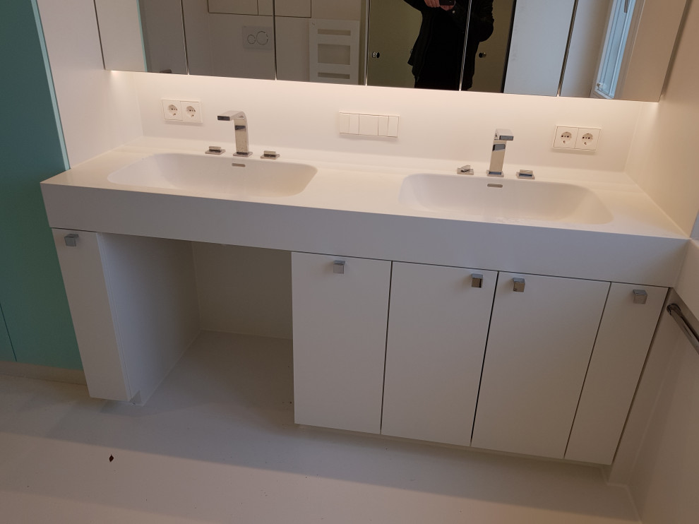 Photo of a large modern 3/4 bathroom in Stuttgart with flat-panel cabinets, white cabinets, a curbless shower, a wall-mount toilet, white tile, porcelain tile, white walls, porcelain floors, an integrated sink, solid surface benchtops, white floor, a hinged shower door, white benchtops, a shower seat, a double vanity, a built-in vanity and wallpaper.