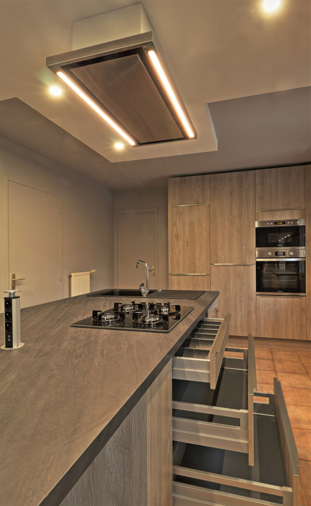 Large modern single-wall eat-in kitchen in Other with an undermount sink, flat-panel cabinets, medium wood cabinets, limestone benchtops, black splashback, slate splashback, stainless steel appliances, limestone floors, with island, brown floor and black benchtop.