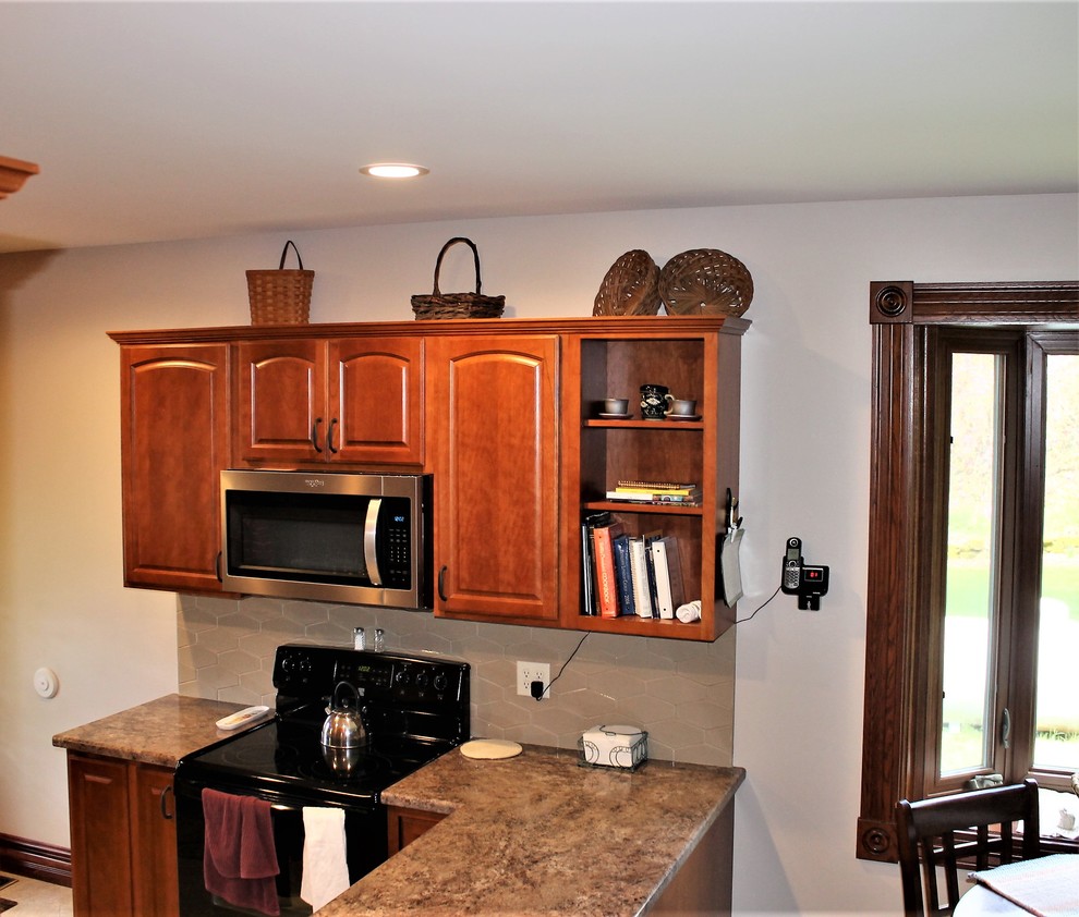 Mid-sized mountain style l-shaped vinyl floor and beige floor eat-in kitchen photo with a farmhouse sink, raised-panel cabinets, medium tone wood cabinets, laminate countertops, beige backsplash, cement tile backsplash, stainless steel appliances, a peninsula and beige countertops