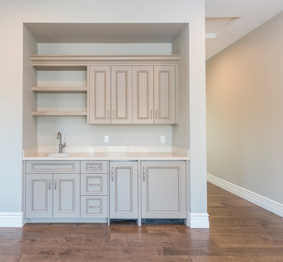 Example of a huge transitional single-wall medium tone wood floor and brown floor wet bar design in Phoenix with an undermount sink, raised-panel cabinets, beige cabinets, marble countertops and beige backsplash