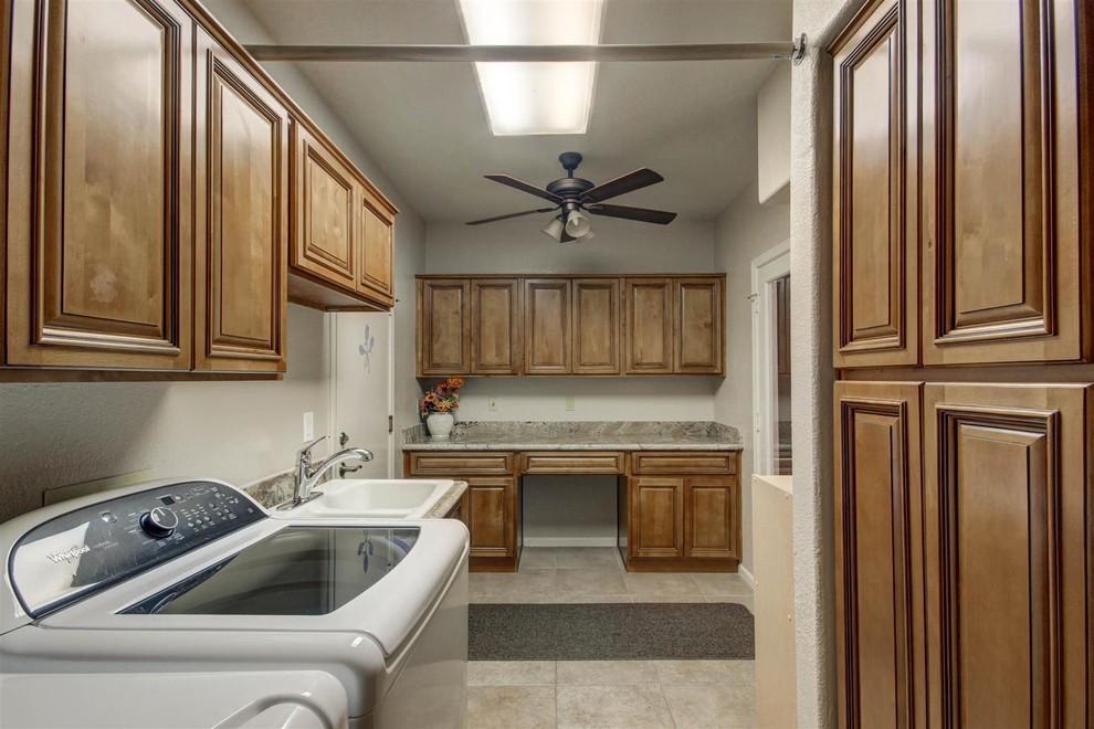 Mid-sized traditional galley utility room in Phoenix with a double-bowl sink, raised-panel cabinets, medium wood cabinets, granite benchtops, beige walls, ceramic floors and a side-by-side washer and dryer.