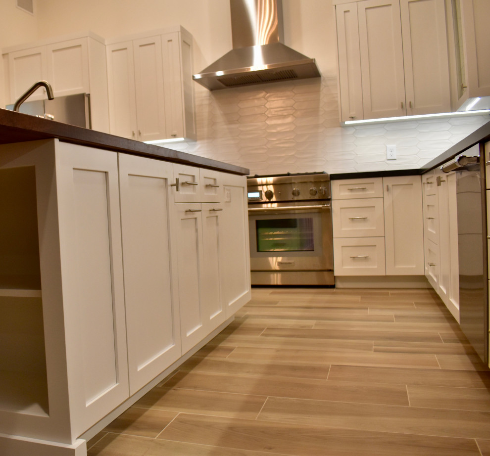 Large transitional l-shaped eat-in kitchen photo with an undermount sink, shaker cabinets, white cabinets, quartz countertops, white backsplash, ceramic backsplash, stainless steel appliances, an island and black countertops