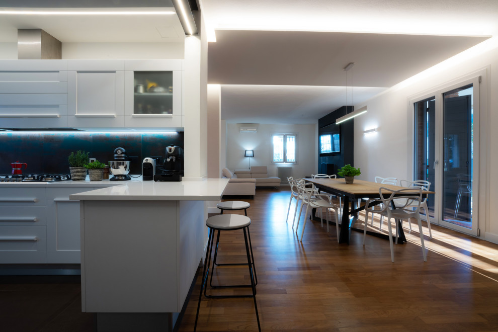 This is an example of a large contemporary u-shaped open plan kitchen in Other with a double-bowl sink, flat-panel cabinets, white cabinets, quartzite benchtops, metallic splashback, porcelain splashback, stainless steel appliances, light hardwood floors, with island, brown floor and white benchtop.