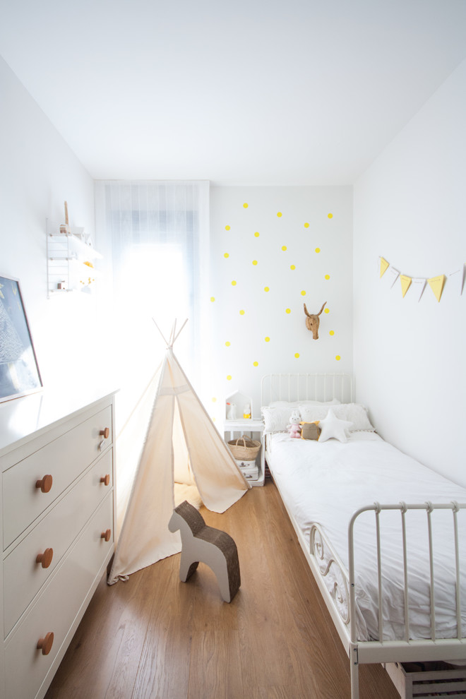 Design ideas for a mid-sized scandinavian gender-neutral kids' bedroom for kids 4-10 years old in Madrid with white walls, medium hardwood floors and brown floor.