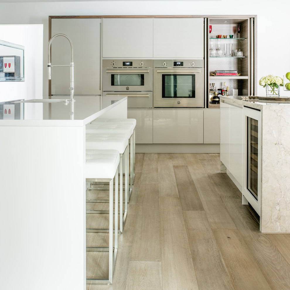 Inspiration for a mid-sized contemporary l-shaped eat-in kitchen in Dallas with an undermount sink, flat-panel cabinets, white cabinets, quartz benchtops, white splashback, stone slab splashback, stainless steel appliances, light hardwood floors and multiple islands.