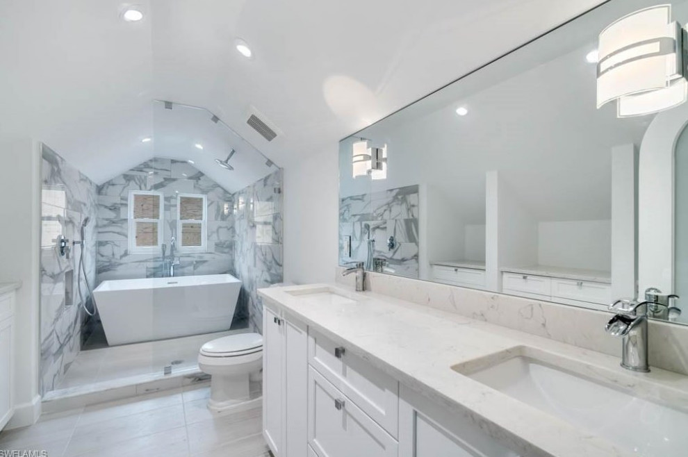 Cette photo montre une salle de bain longue et étroite chic avec un placard à porte shaker, une baignoire indépendante, du carrelage en marbre, aucune cabine, meuble double vasque et un plafond voûté.