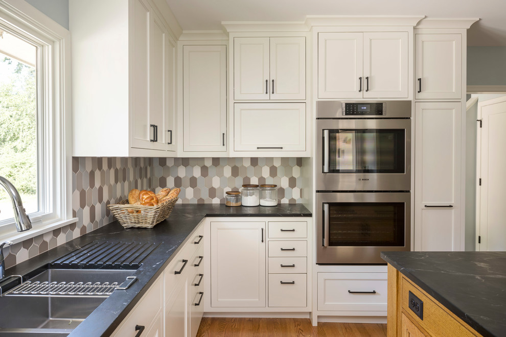 Kitchen - mid-sized transitional u-shaped medium tone wood floor and brown floor kitchen idea in Minneapolis with an undermount sink, recessed-panel cabinets, white cabinets, granite countertops, multicolored backsplash, ceramic backsplash, stainless steel appliances and an island