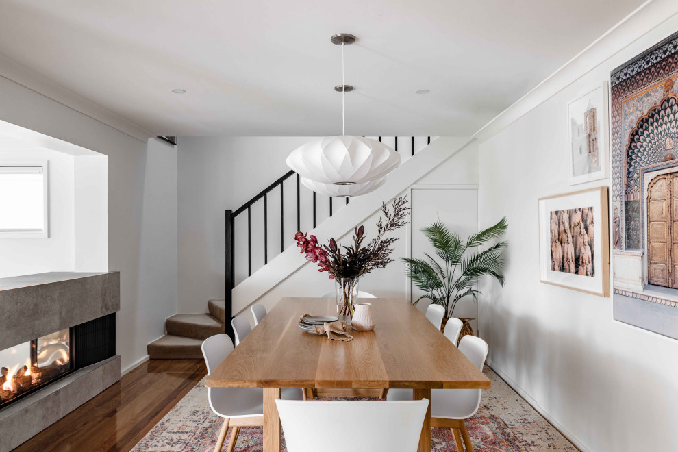 Photo of a mid-sized contemporary kitchen/dining combo in Sydney with white walls, light hardwood floors, a two-sided fireplace, a tile fireplace surround and brown floor.