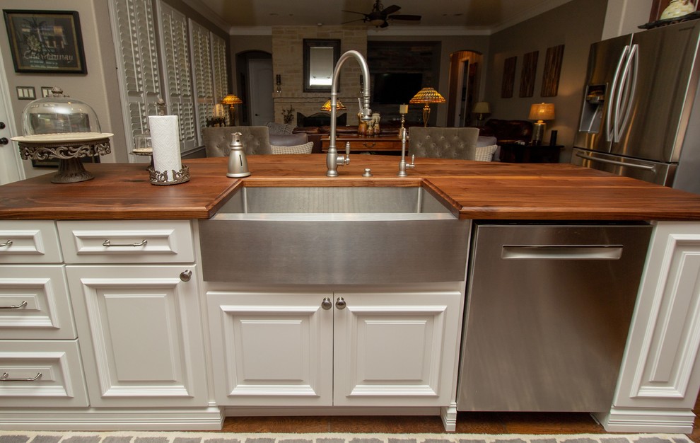 Example of a mid-sized farmhouse l-shaped medium tone wood floor and brown floor open concept kitchen design in Houston with a farmhouse sink, raised-panel cabinets, white cabinets, wood countertops, white backsplash, subway tile backsplash, stainless steel appliances, an island and brown countertops
