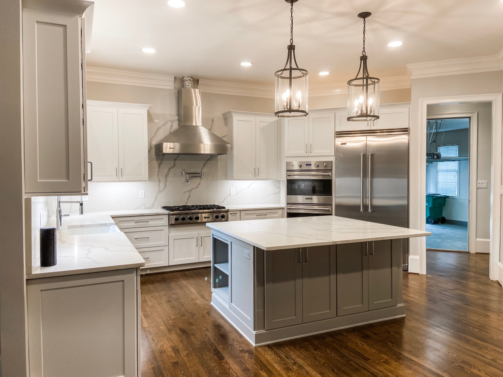 This is an example of a large transitional l-shaped open plan kitchen in Atlanta with a farmhouse sink, shaker cabinets, white cabinets, quartz benchtops, white splashback, engineered quartz splashback, stainless steel appliances, dark hardwood floors, with island, green floor and white benchtop.