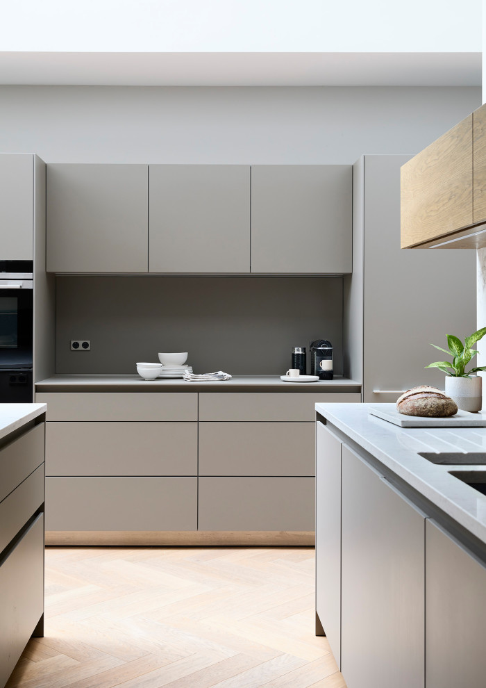 Design ideas for a contemporary kitchen/diner in Other with a double-bowl sink, flat-panel cabinets, beige cabinets, engineered stone countertops, white splashback, engineered quartz splashback, black appliances, light hardwood flooring, an island, beige floors and white worktops.