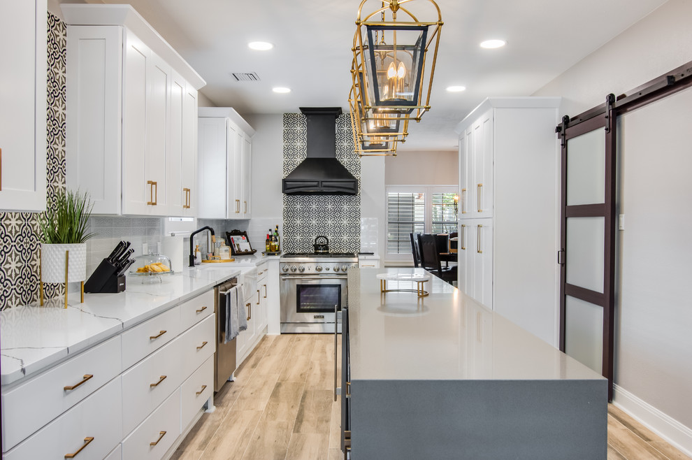 Inspiration for a large transitional l-shaped porcelain tile and brown floor kitchen remodel in Houston with a farmhouse sink, shaker cabinets, white cabinets, quartzite countertops, glass tile backsplash, stainless steel appliances, an island, white countertops and multicolored backsplash