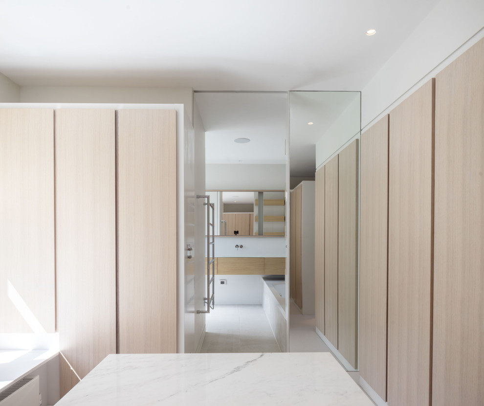 Foto di un ampio spazio per vestirsi unisex moderno con ante lisce, ante in legno chiaro, pavimento in marmo e pavimento bianco
