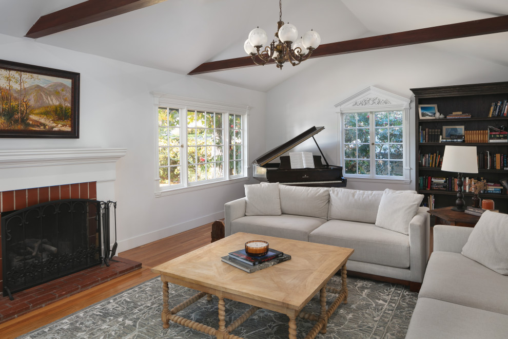 Mid-sized transitional formal enclosed living room in Los Angeles with white walls, medium hardwood floors, a standard fireplace, a brick fireplace surround, a concealed tv, brown floor and vaulted.